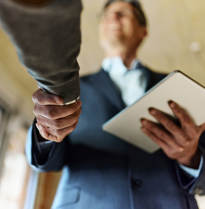 A businessman in a suit shaking hands with another person, holding a tablet, symbolizing a successful business agreemen